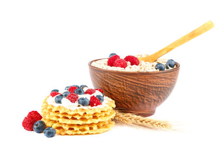 Fresh blueberries, raspberries, waffle cookies and oatmeal in a bowl with a wooden spoon isolated on a white background.の写真素材