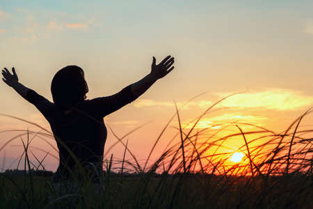 A young beautiful girl raised her hands to the sky at sunset.の写真素材