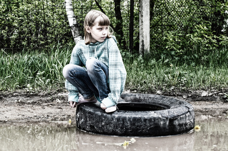 Girl sitting on a wheel that lies in a puddle on the road near the forestの写真素材