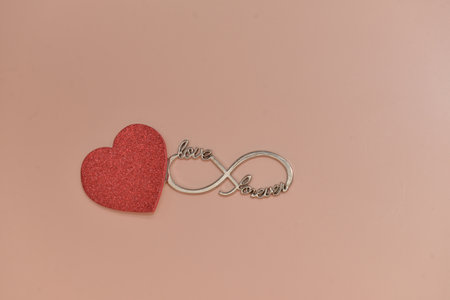A close-up shot of a pink glitter heart and an infinity symbol on a beige background. Highlights the...