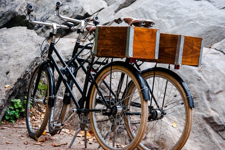 Photograph of two retro bikes leaning against one another in front of a large rock の写真素材