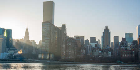 New York skyline taken from the east river near sunset with light rays shining through buildingsの写真素材