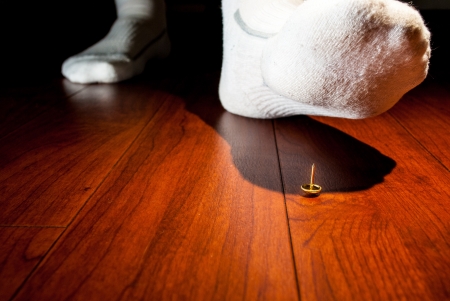 Photograph of a human foot about to step on an upright tack on a wooden floor.の写真素材