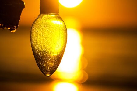 Photograph of a Christmas Ornament found hanging on a beach backlit by rising sun over ocean.の写真素材
