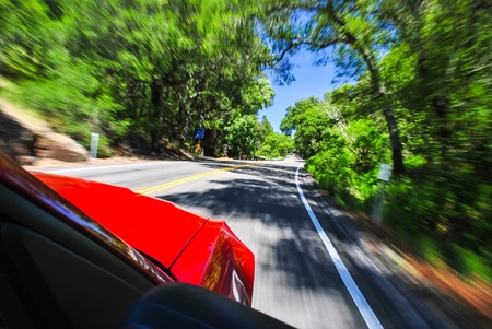 Photograph of a red sports car flying down a back country road with trees and road blurred.の写真素材
