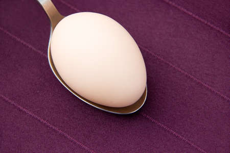 Chicken egg is on burgundy cloth in a metal spoon close-up.の写真素材