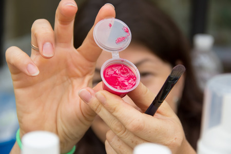 Cosmetic jar with bright lipstick and brush in female hands close up.の写真素材