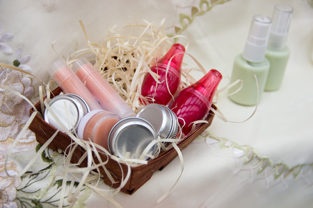 Four jars of cream, two lipsticks, two lip balm in a bright jar in a basket of bast are on the tablecloth.の写真素材