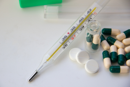 Thermometer with a temperature of 38 and tablets and capsules on a white backgroundの写真素材