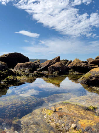 A small water pond with clear reflection surrounded by sea rocks at the coast next to the sea, Palm Beach NSW Australiaの写真素材