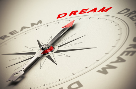 Compass with red needle pointing the word dream, beige paper background, symbol of achieving dreams