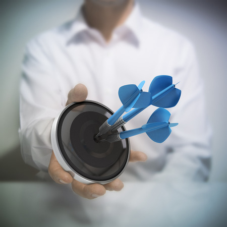 Man holding on black target with three blue darts hitting the center.