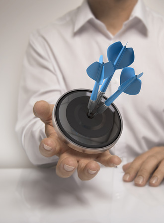 Man hand holding a target with three darts hitting the center, blue and beige tones, concept image for illustration of marketing or business solutionsの写真素材