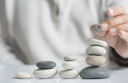 Horizontal image of a man stacking pebbles on a table with copyspace for text. Concept of risk management and wealth.の写真素材
