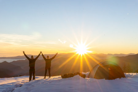 Couple celebrating next to tent in snow at sunsetの写真素材