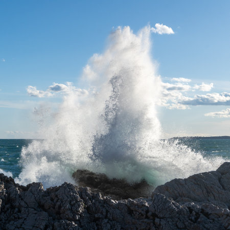 Waves crashing at cliff in sunlightの写真素材