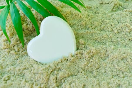 White porcelain heart and palm branch, lies on the sea sand. The concept of a summer holidayの写真素材