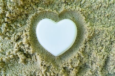 White porcelain heart and palm branch, lies on the sea sand. The concept of a summer holidayの写真素材