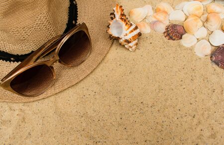 Summer vacation concept with seashells, women's beach hat and sunglasses on sand background. Flat...