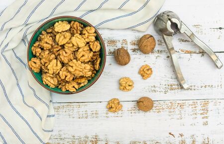 Peeled walnuts in a plate and nut cracker on a light wooden background. View from above.