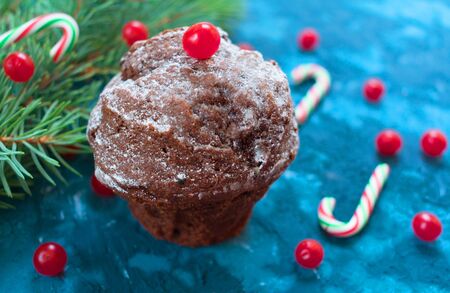 Christmas homemade chocolate muffin decorated with red berries and sweets on the background of a Christmas tree branch.の写真素材