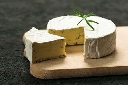 Camembert cheese with greens decorated with a sprig of rosemary on a wooden board on a black background.の写真素材