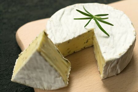 Camembert cheese with greens decorated with a sprig of rosemary on a wooden board on a black...