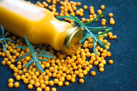 A bottle of vitamin juice from sea buckthorn and fresh berries of sea buckthorn on a black background. Close-up.の写真素材