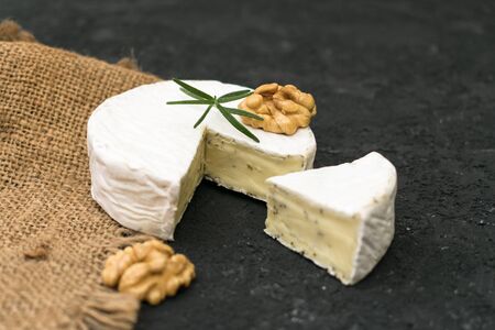 Camembert cheese with herbs, decorated with a sprig of rosemary and walnut on a black background.の写真素材