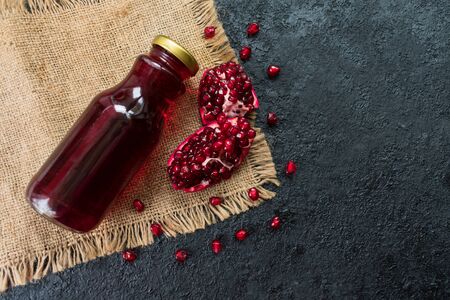 Pomegranate juice in a bottle and pomegranate on a black background. Flat lay. Vitamin drink. Copy space.の写真素材