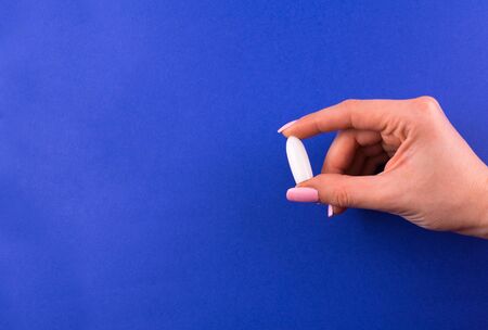 White suppository for anal or vaginal use in a female hand on a blue background. Copy space