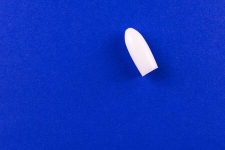 One suppository (candle) for anal or vaginal use on a blue background. Medetsyn candles. Copy space.