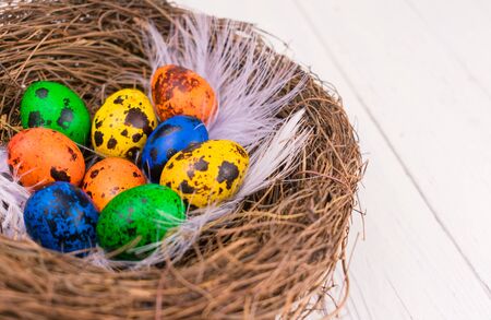 Multi-colored Easter eggs in a nest on a white wooden background.