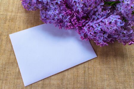A bouquet of lilac flowers in a lilac vase and an envelope. Postcard. Copy spaceの写真素材