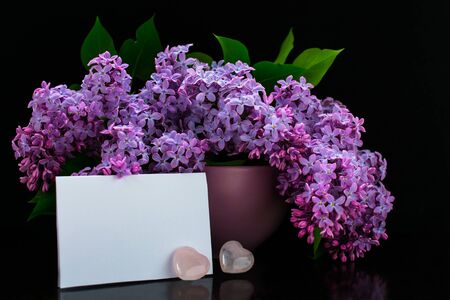 A bouquet of lilac flowers in a lilac vase, small pink hearts and a pure krnvert on a black background. Card. Copy spaceの写真素材