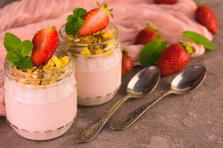 Two jars of yogurt with strawberries and granola on a gray table. Close-up.の写真素材