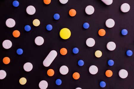 Background from multi-colored pills. Tablets on a black background. Flat lay.