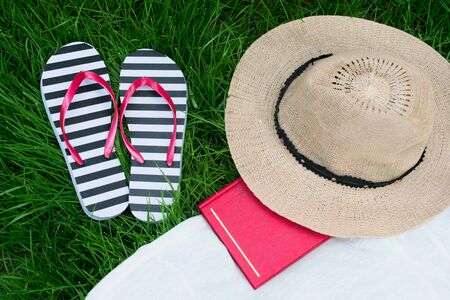 Sun hat book flip flops on green grass. Summer vacation concept.の写真素材