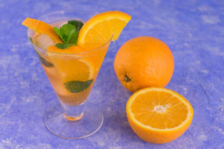 A glass of refreshing orange cocktail with mint and ice on a blue bright background.の写真素材