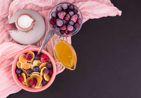 Breakfast of small pancakes with berries and honey, decorated with mint on a black background. Pancake porridge. Copy space.の写真素材