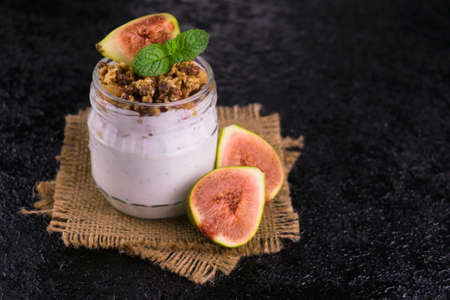 Yogurt with figs and granola in a jar on a black background.の写真素材