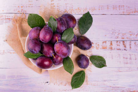 Blue plums in a plate on a  wooden table.