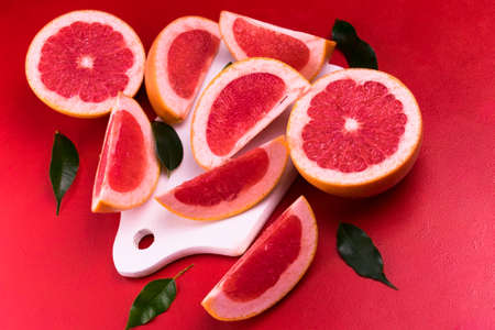 Grapefruit and wedges with leaves, on a red background. View from above. Flat lay.