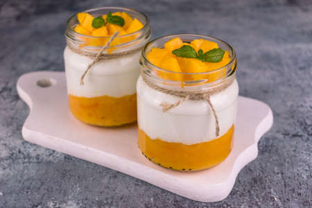 Two servings of yogurt with mango on a white wooden board.の写真素材