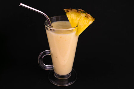 Pineapple banana smoothie in a glass on a black background.