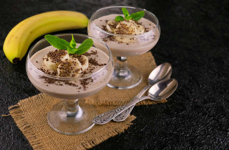Banana cream dessert decorated with chocolate chips and mint on a black background. Copy space.の写真素材