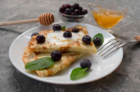 Pancakes with berries and honey in a white plate.