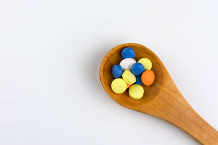 Lots of multicolored pills in a wooden spoon on a white background.Copy space.の写真素材