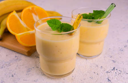 Two glasses of orange banana smoothie with a mint leaf on a white background.の写真素材