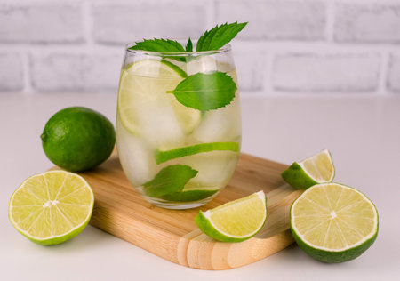 Glass of ice green tea with lime and mint on a wooden board.